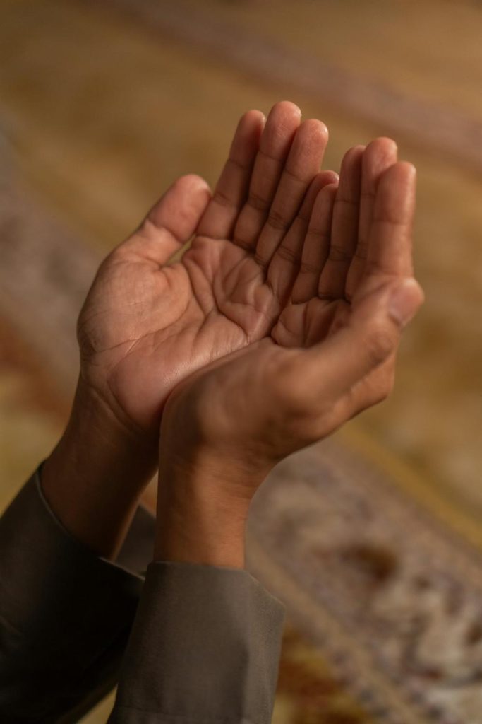 Hands raised in dua over a patterned prayer rug