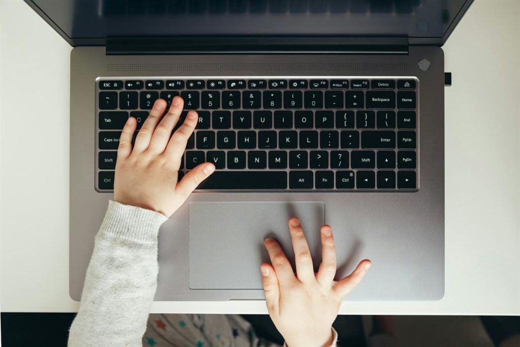 A child's hands typing on a laptop during a live online Quran lesson