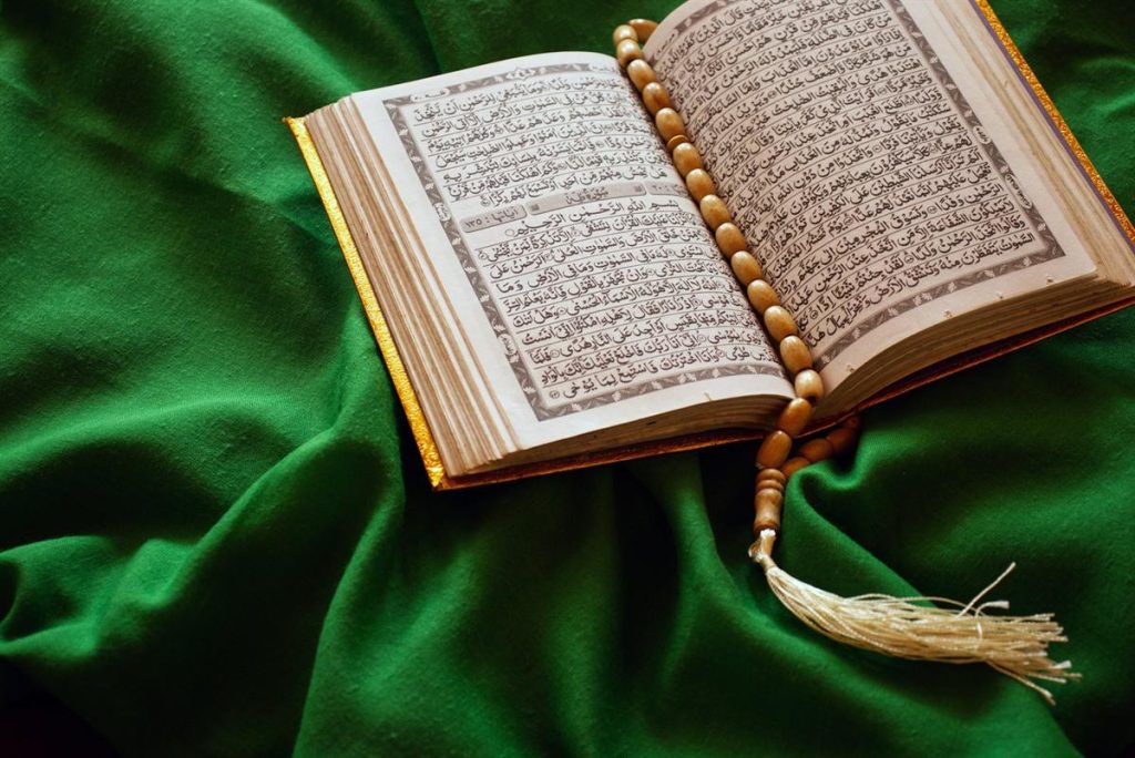 An open Quran with prayer beads resting on green silk