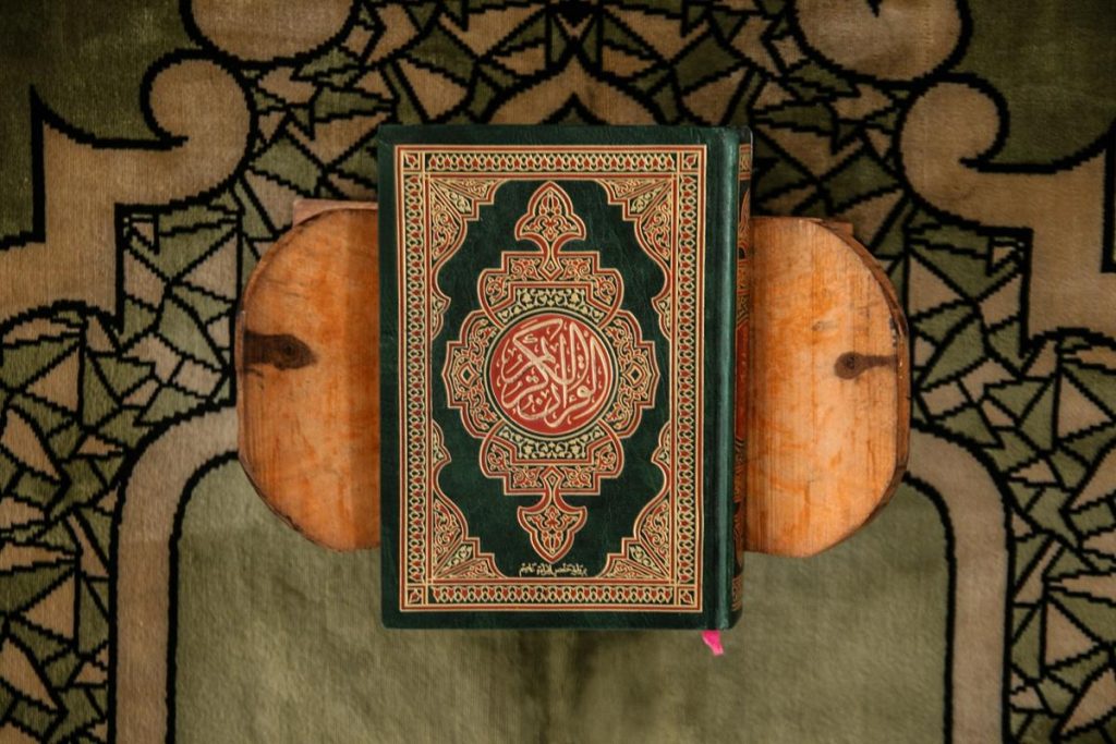 A Quran on a wooden stand placed over a patterned prayer rug
