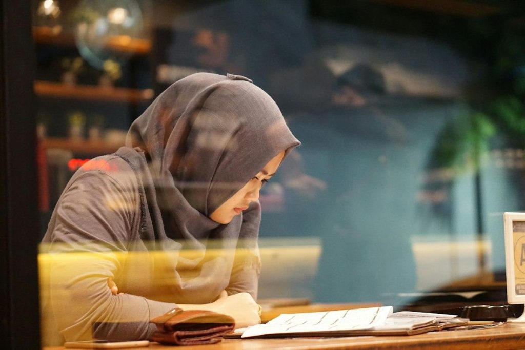 A young woman in a hijab reading and studying at a desk