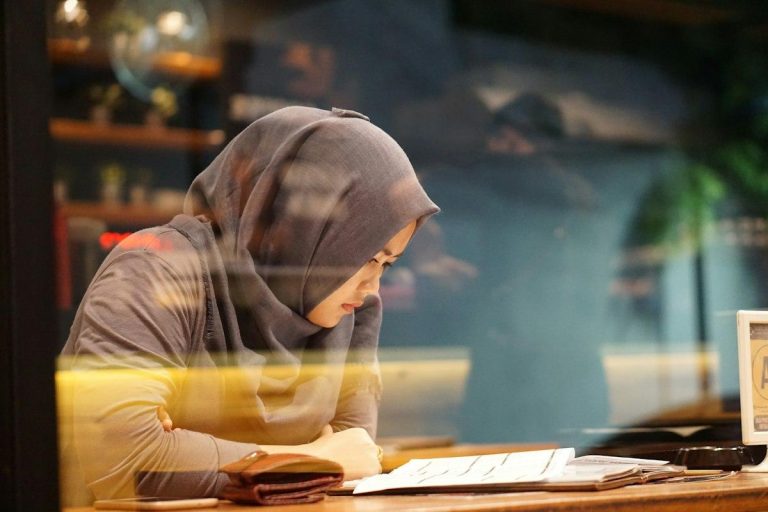 A young woman in a hijab reading and studying at a desk